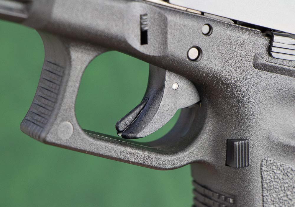 In this photo, we see a detailed look at the Glock 17 Gen 3 trigger. Glocks - from the very first model to the Gen 5 - use a trigger safety which is a thin blade in the center of the trigger shoe that allows you to pull it to the rear which then discharges the firearm. Every Glock Gen incorporates the same basic safety. I have one on my Glock 19 and the newest Glock 17 Gen 5 has it as well. Aftermarket triggers are available with a smooth face, but I like it the way it is for home defense as well as police and military use. There are dozens of different opinions on how hard to go with this, but I like to keep mine stock.